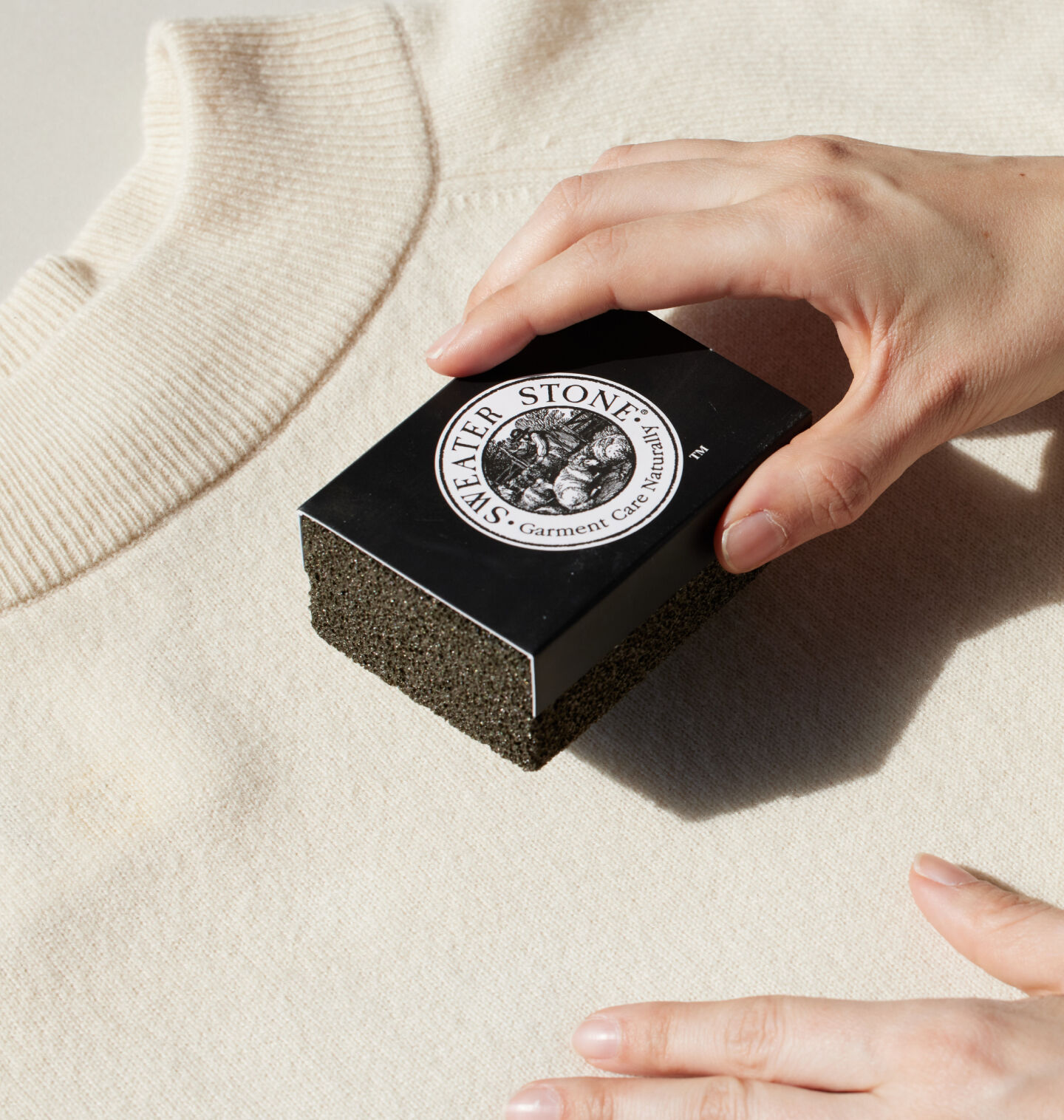 Hand using a sweater stone to depill a sweater. Hand using a sweater stone to depill a sweater.