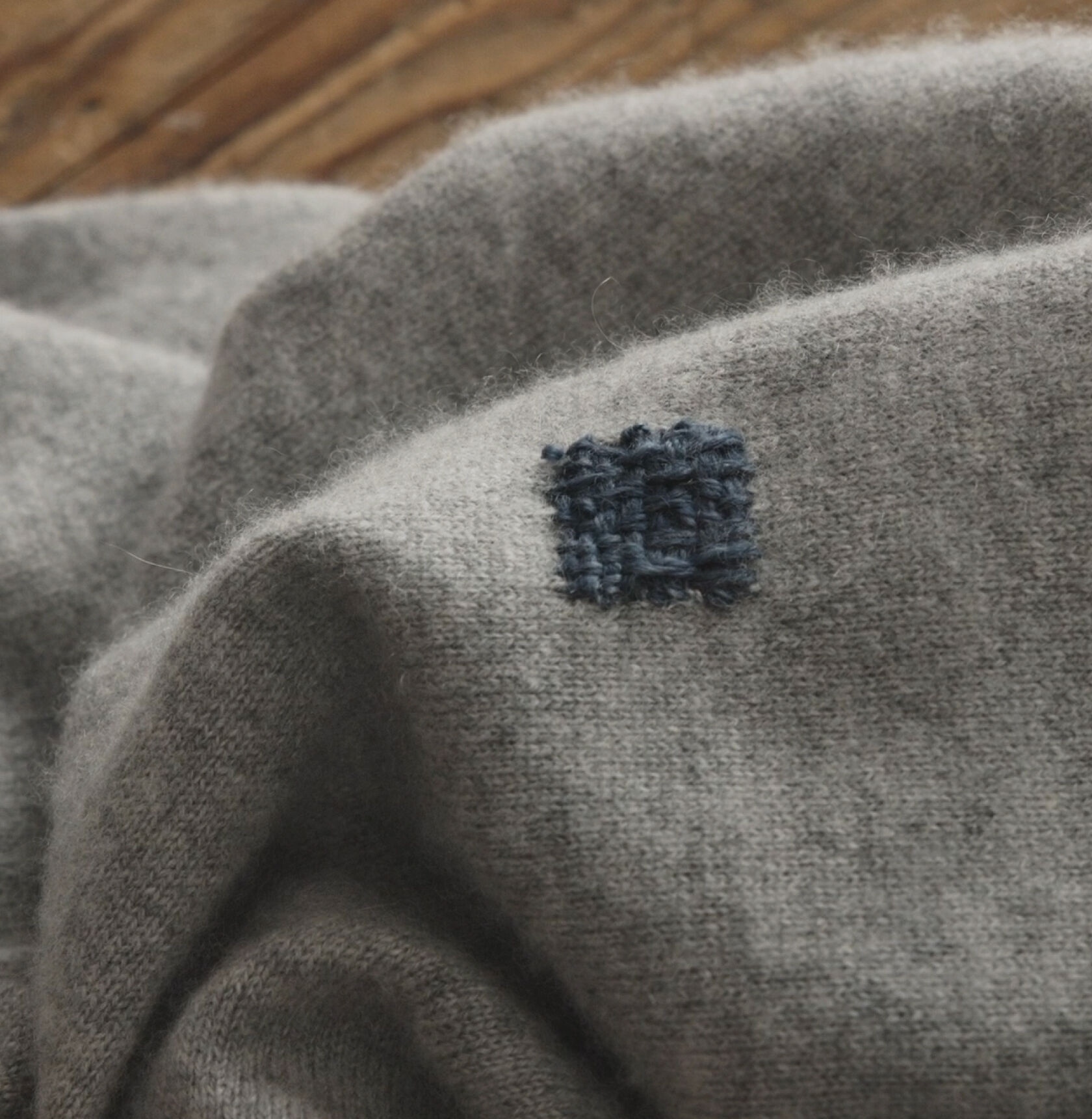 Completed blue thread visible repair square on gray sweater. Completed blue thread visible repair square on gray sweater.