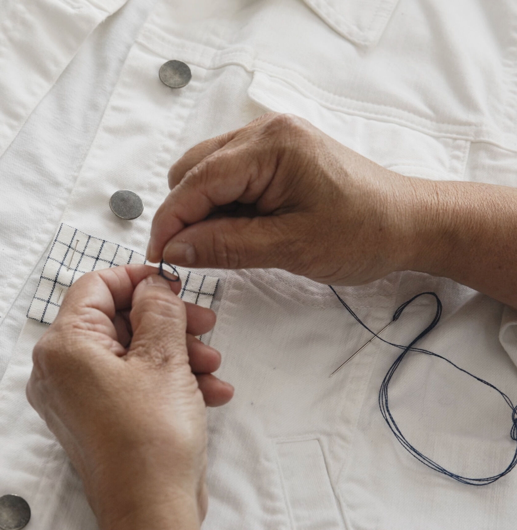 Hands threading a needle with blue thread. Hands threading a needle with blue thread.