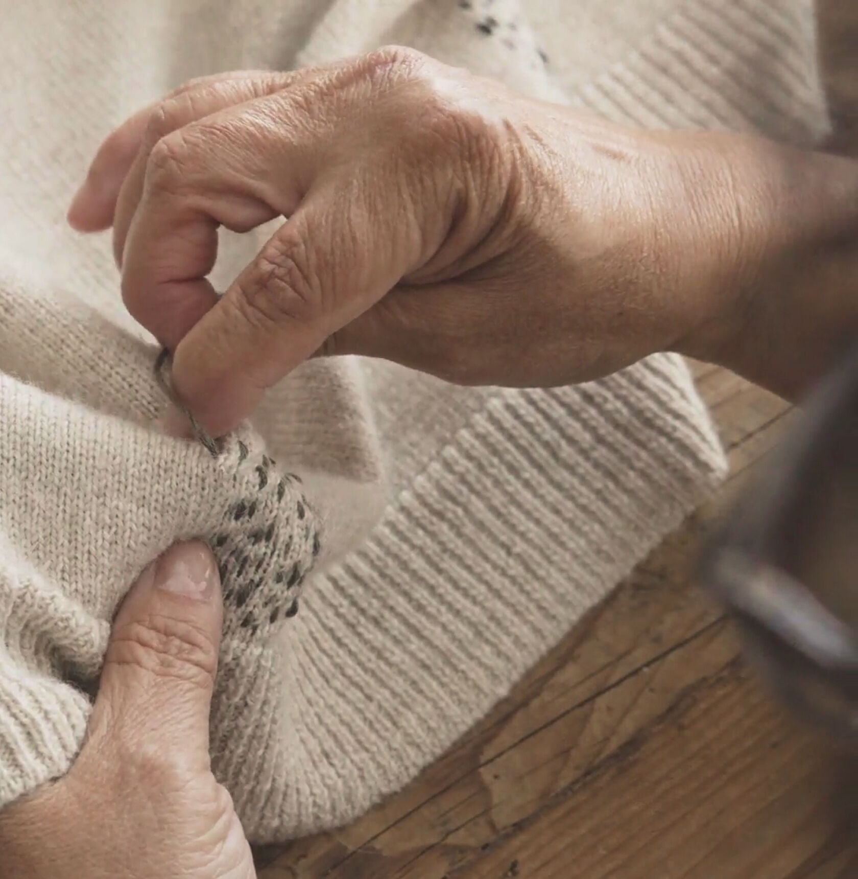Hands creating a stitching pattern using contrasting thread on a beige sweater. Hands creating a stitching pattern using contrasting thread on a beige sweater.