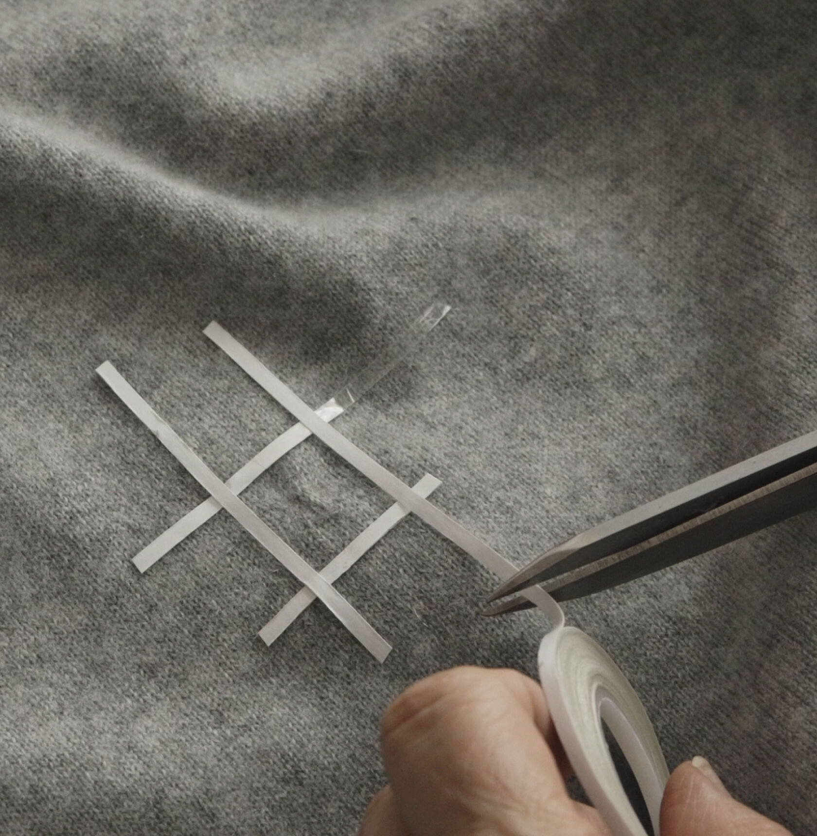 Close-up of hands taping a small square on a gray sweater. Close-up of hands taping a small square on a gray sweater.