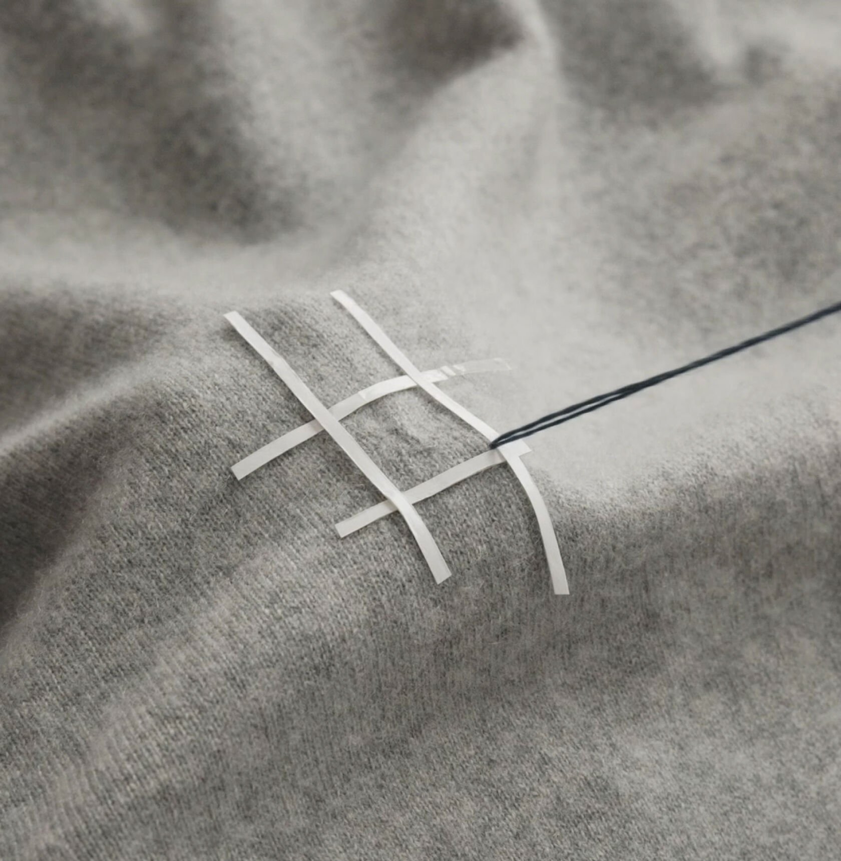 Close-up of hands stitching with a blue thread on a gray sweater. Close-up of hands stitching with a blue thread on a gray sweater.