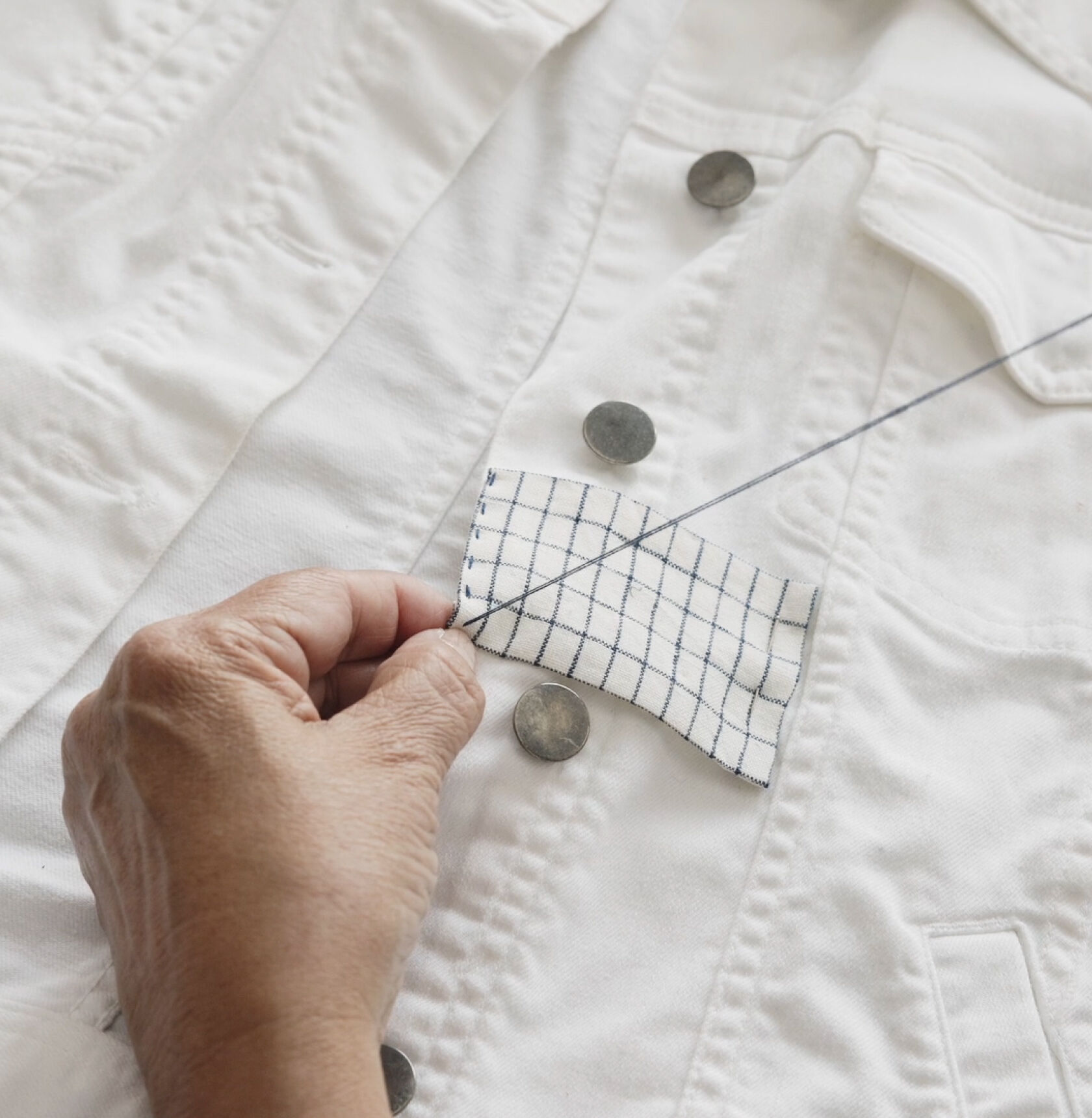 Hands stitching a patch on white denim jacket. Hands stitching a patch on white denim jacket.