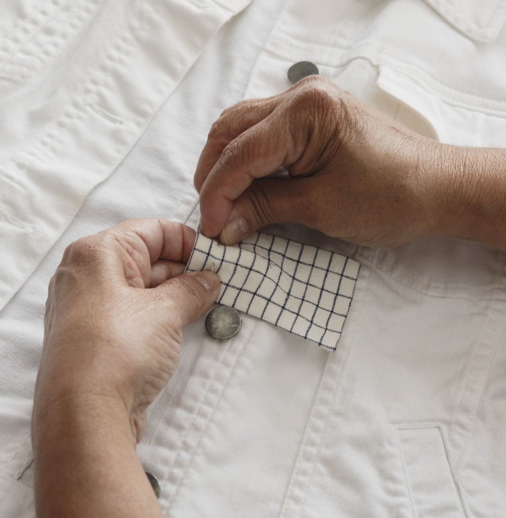 Hands pinning a fabric patch on white denim jacket. Hands pinning a fabric patch on white denim jacket.