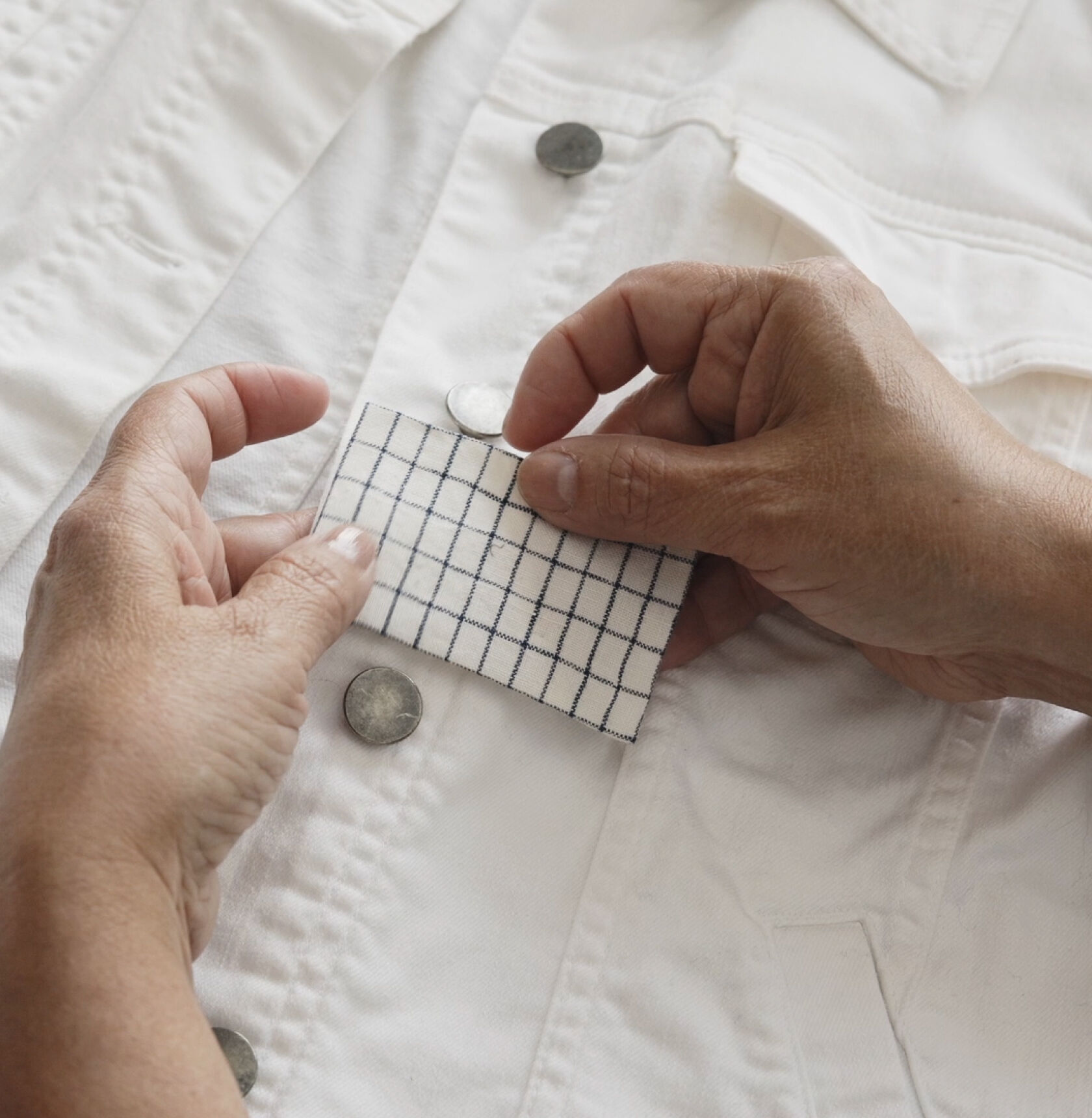 Hands holding a fabric patch against white denim jacket. Hands holding a fabric patch against white denim jacket.
