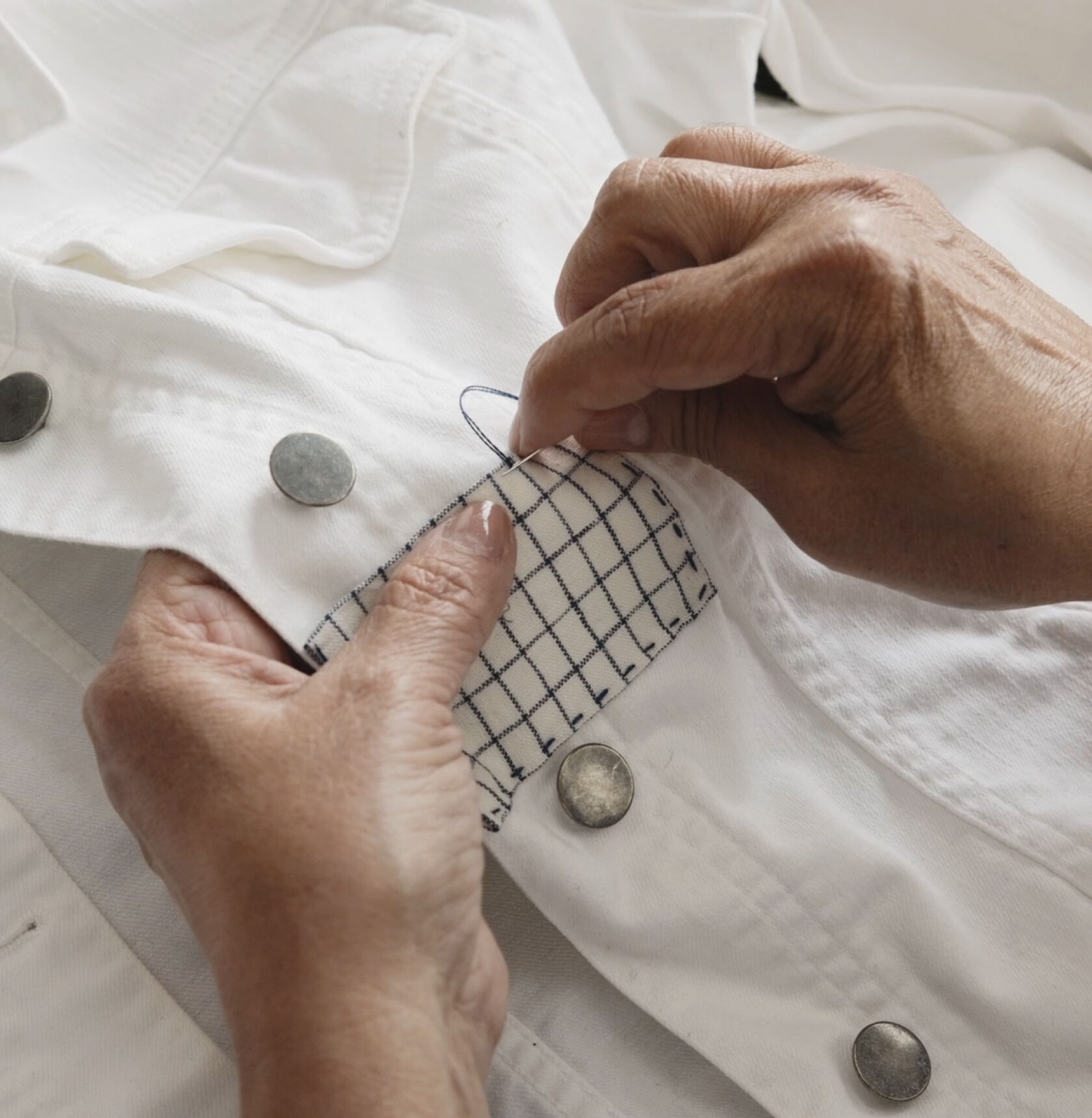 Hands making final stitches on a rectangular fabric patch. Hands making final stitches on a rectangular fabric patch.