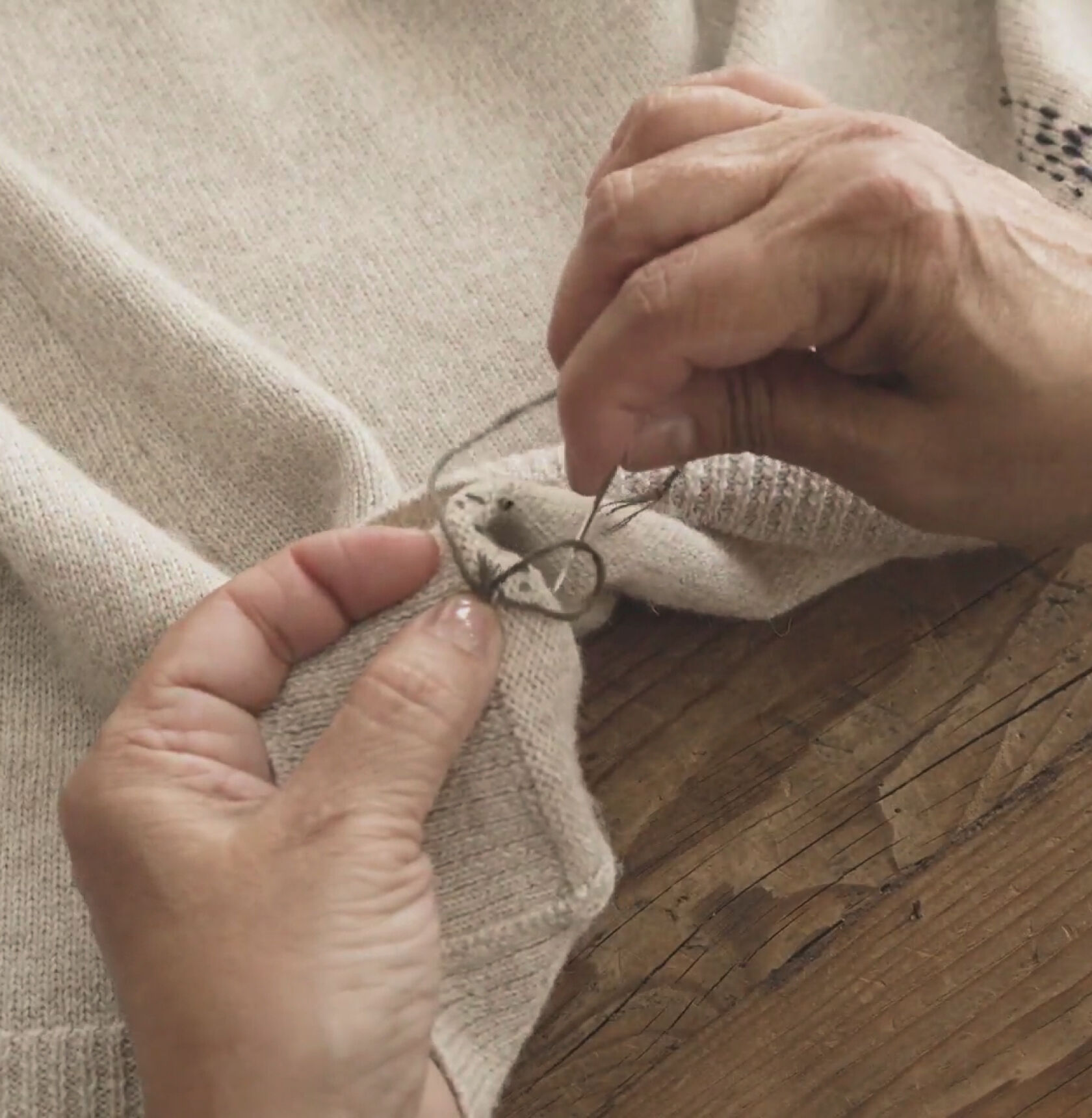 Hands knotting thread on the underside of a beige sweater. Hands knotting thread on the underside of a beige sweater.