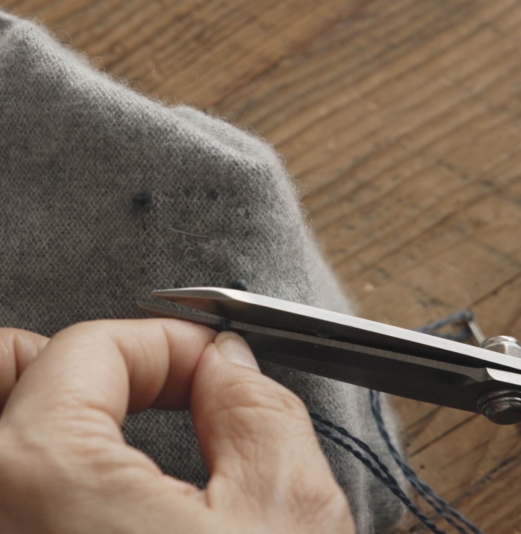 Tying off blue thread on a mended gray sweater. Tying off blue thread on a mended gray sweater.