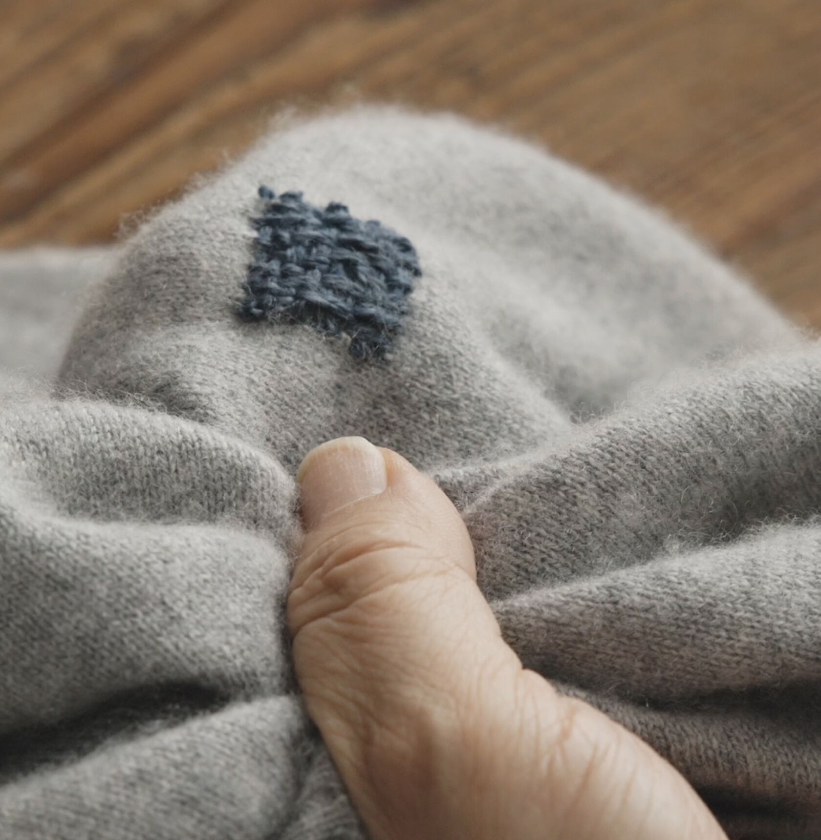Close-up of a blue embroidered square on a mended gray sweater. Close-up of a blue embroidered square on a mended gray sweater.