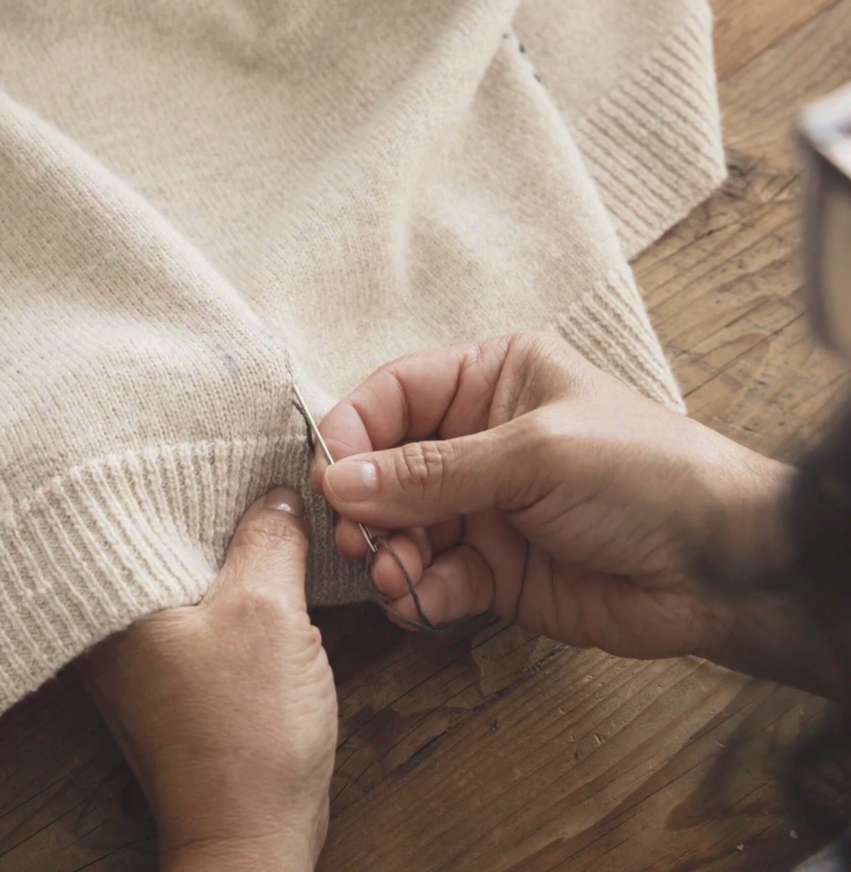 Hands doing a running stitch with a contrasting thread on a beige sweater. Hands doing a running stitch with a contrasting thread on a beige sweater.
