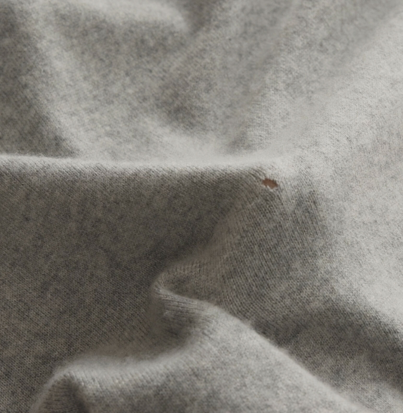 A gray sweater with a small moth hole. A gray sweater with a small moth hole.